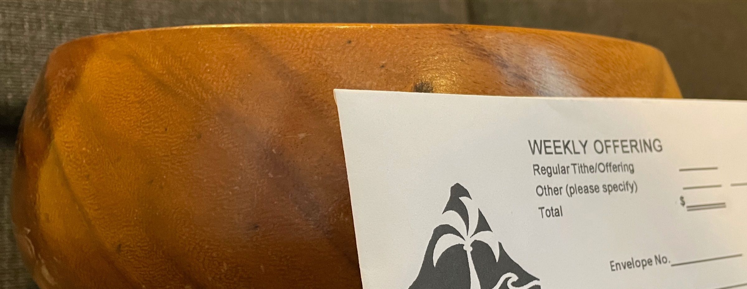 A wooden offering bowl with a Hawaiʻi Kai Church weekly offering envelope